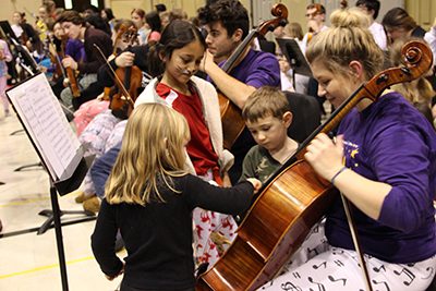 Elementary Students playing instrument with high school student